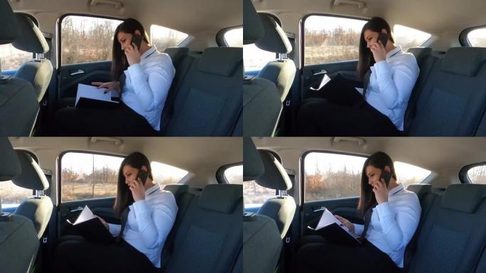 一位年轻的女商人坐在汽车的后座上-她正在出差的路上，他使用平板电脑电话，翻阅文件，进行约会并在旅行时