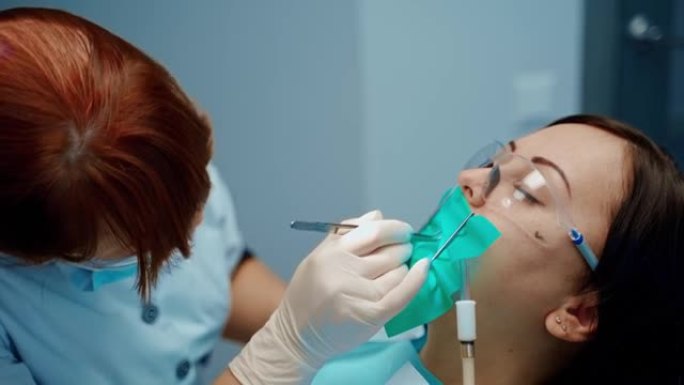 牙科椅上戴着防护眼镜的病人的脸。在牙科中心治疗女性牙齿的专业口腔科医生。口腔医学概念。