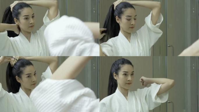 美丽的年轻女子站在浴室镜子前扎着马尾辫的头发准备。