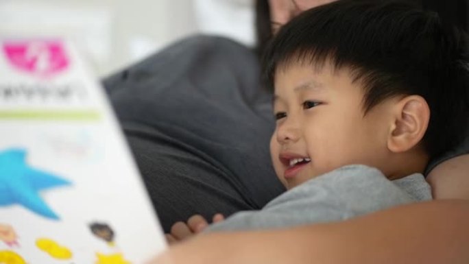 亚洲孩子和母亲在卧室里看书睡前故事。家庭时间的概念