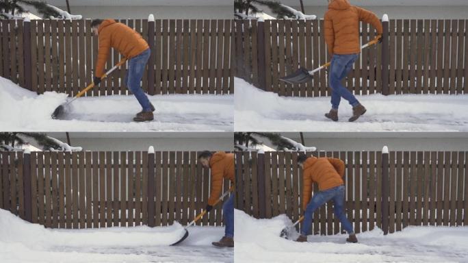 一名男子用雪铲从栅栏附近的道路上铲雪。