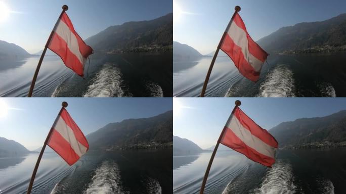 奥地利国旗安装在船轨的民意测验上。旗帜在风中轻轻地挥舞着。湖面四面环绕着高山，宁静而平静。乘船游览