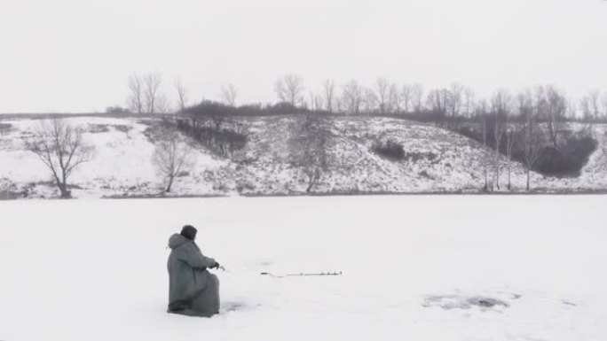 冬季钓鱼。穿着冬季极端服装的渔夫正在冰冻的湖上抓鱼。冬季自由日，有钓鱼竿的人在冰洞里钓鱼