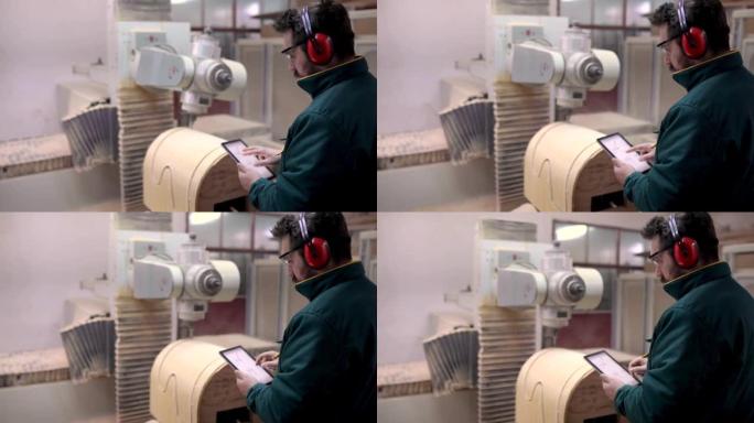 木匠戴着耳罩，通过数码板，在工厂调整和打开数控机床