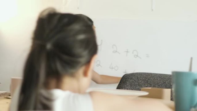 亚洲女孩在新型冠状病毒肺炎期间在家为姐姐在白板上教数学，社交距离概念。