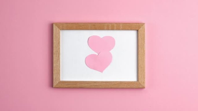 在中间的粉红色背景上的木制框架中的粉红色纸心的停止运动动画。情人节，母亲节爱情关系浪漫周年婚礼节日概