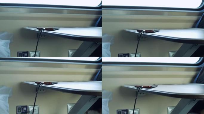 在行驶中的车辆中，智能手机在桌子上，并且正在从火车上特殊插座中的充电器充电。特写