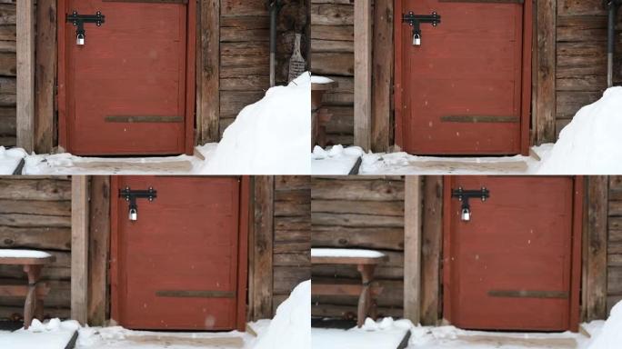 木头圆木墙上的旧谷仓门。下雪了。