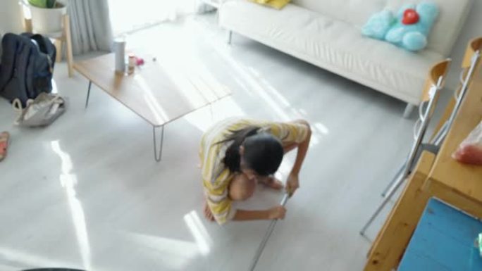 亚洲女孩在家用拖把自己打扫客厅，生活方式理念。