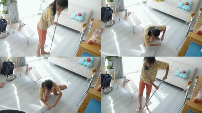 亚洲女孩在家用拖把自己打扫客厅，生活方式理念。