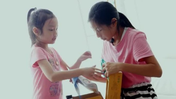 快乐的亚洲儿童收到了网上购物的商品，并在家里的窗户附近打开了棕色盒子，生活方式理念。