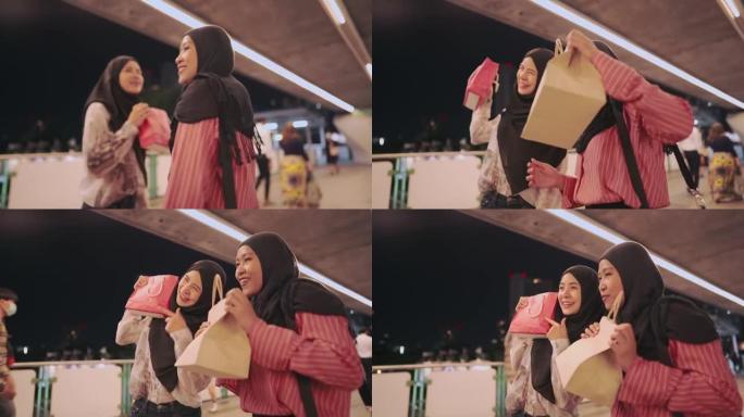 两个年轻的亚洲穆斯林朋友很高兴向相机展示购物袋，现代穆斯林生活方式，资本主义消费者花钱，打折销售产品