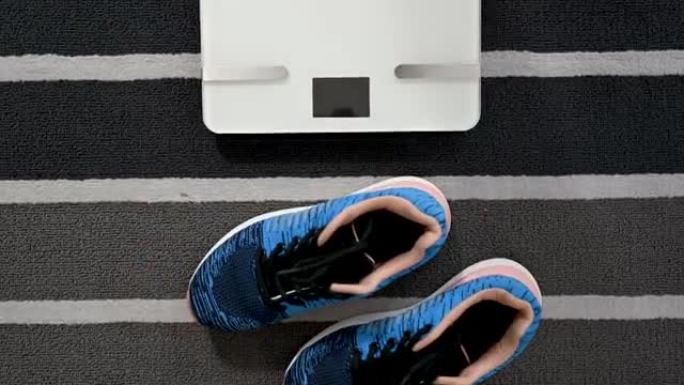 体重秤上的女人测量体重。女孩的腿踩在浴室秤上。关闭女性检查BMI体重减轻。饮食，减肥和健康的生活方式