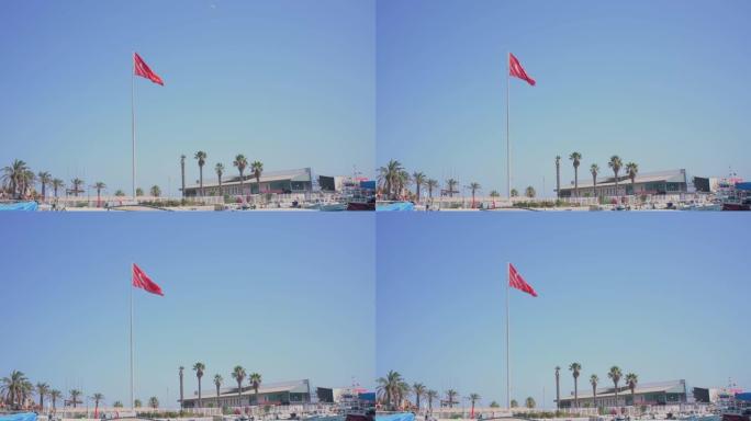 红色土耳其国旗在带有渔船的城市码头下的湛蓝天空中挥舞。