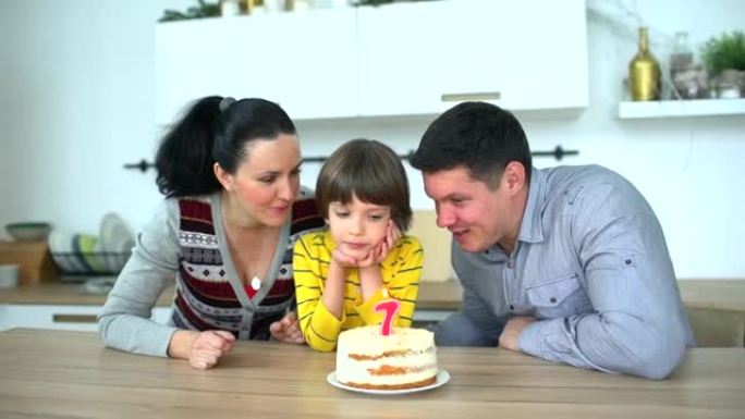 非常可爱的男孩用蛋糕庆祝他的生日 & 快乐的父亲和母亲。7年。小男孩在家吹灭生日蛋糕上的蜡烛。快乐的