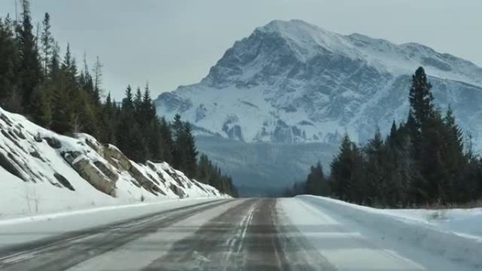 在加拿大艾伯塔省贾斯珀和班夫国家公园的加拿大落基山脉，一辆汽车驶过森林的雪地道路的驾驶员透视图