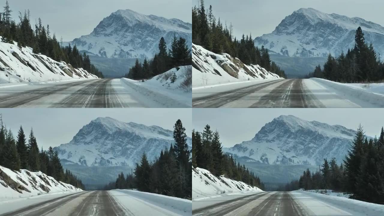 在加拿大艾伯塔省贾斯珀和班夫国家公园的加拿大落基山脉，一辆汽车驶过森林的雪地道路的驾驶员透视图