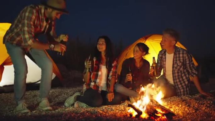 穿着休闲装的年轻成年男子在帐篷露营的海滩篝火晚会上给他的朋友带来了四瓶啤酒