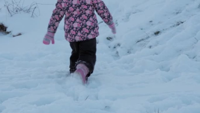 冬季，假期，游戏，家庭概念-慢动作特写婴儿在深雪中行走。孩子们的脚踩在雪道上。寒冷季节的降雪中穿着黑