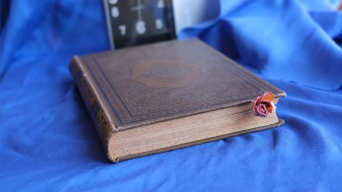 时间概念。旧书和玫瑰。一本古董书和一朵干玫瑰，背景是一个移动的时钟指针
