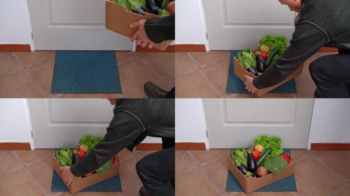 在检疫和大流行期间，一名送货员将一盒新鲜蔬菜放在门前的地板上。食品供应概念。