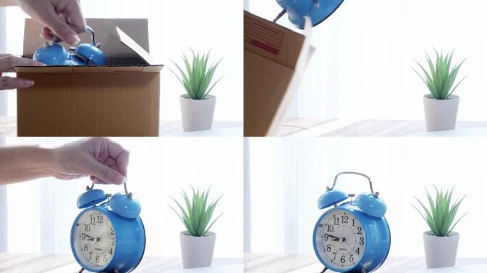 双手从棕色盒子里拿起蓝色的闹钟，放在家里窗户附近的桌子上，磨练网上购物的概念。