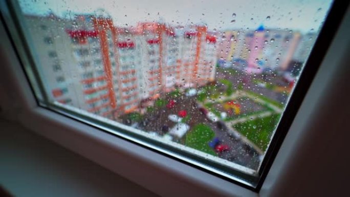 透过窗户看下雨的天气。城市建筑背景窗玻璃上的雨滴。玻璃上流动的雨滴。