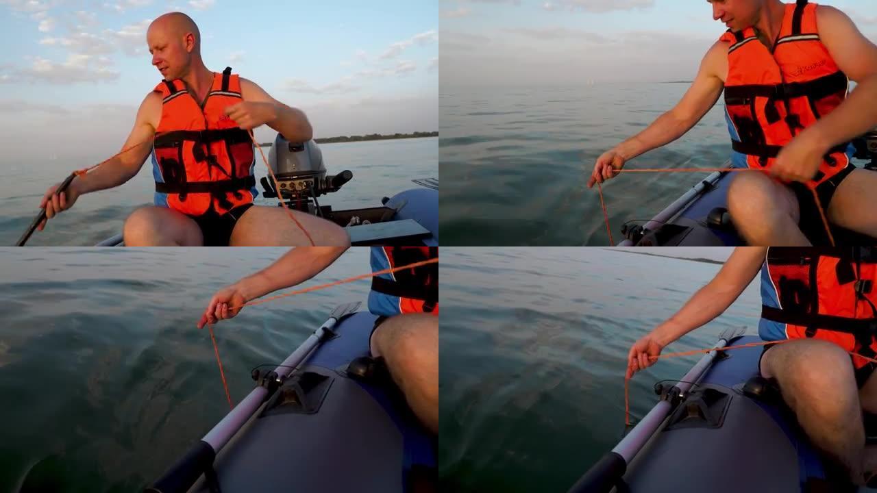一名身穿救生衣的成年男子在机动橡胶充气船上放下水中的锚，并测量海湾的深度。停下来钓鱼。在河上乘船旅行