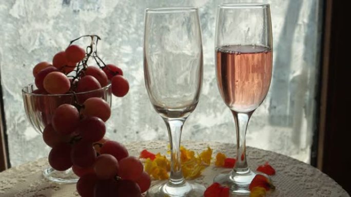 粉红色的葡萄酒，倒入酒杯中，一束粉红色的葡萄放在带有冰花的窗户的花瓶中