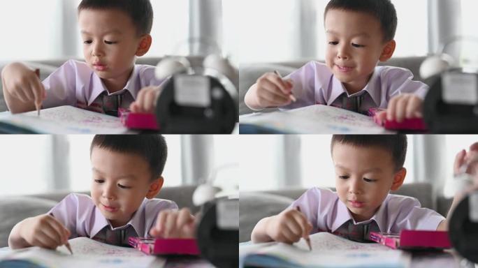 亚洲男孩用心做作业。男孩拿着铅笔写字，男孩在桌子上的白纸上画画，小学和家庭教育，远程在线教育概念。