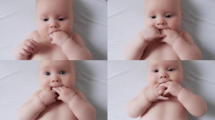 专注可爱的幼儿把手放在嘴里咀嚼手指躺在舒适的白色床单上
