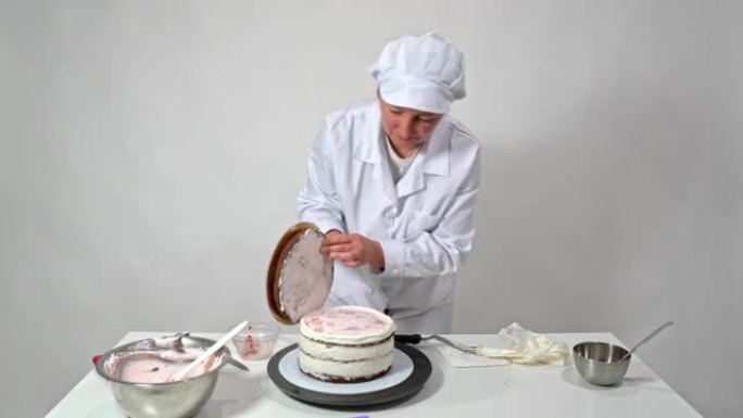一位穿着白色长袍的面包师妇女将蛋糕的最后一层放在糖奶油上。烘焙用糖果。