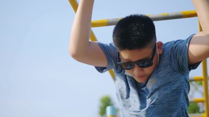 快乐的亚洲男孩在阳光明媚的日子里戴着墨镜在操场上玩耍，生活方式理念。