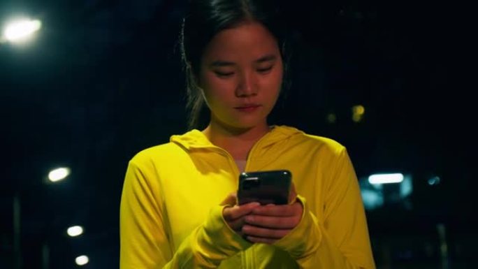 晚上在市区进行锻炼训练后，女运动员使用智能手机。