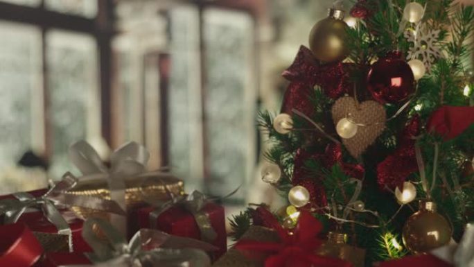 新年圣诞节背景，背景上有霜冻的窗户和飘落的雪。圣诞树，礼物。装饰品，红色的金球，发光的灯泡。温暖的家