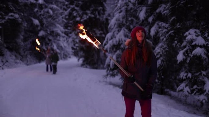 十几岁的女孩和她的家人带着火炬在冬季森林中行走