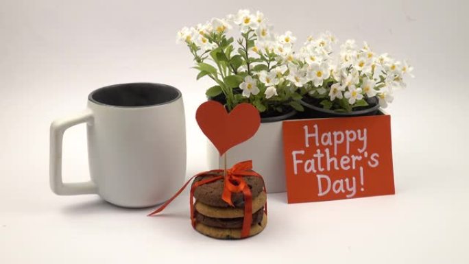 纪念父亲节的贺卡，樱草花，一杯茶和一个节日饼干站在白色的桌子上