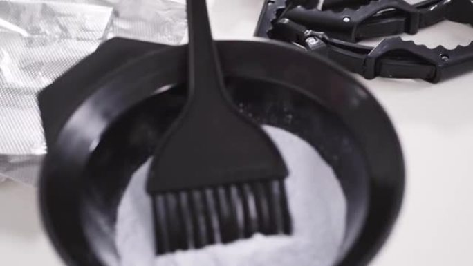 染发剂粉末在白色背景上的黑色塑料搅拌碗中。