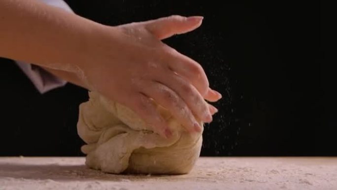 女人的手在桌子上揉面粉。用面粉制作手工面团的过程。制作面包、烹饪烘焙和糖果。特写，慢动作
