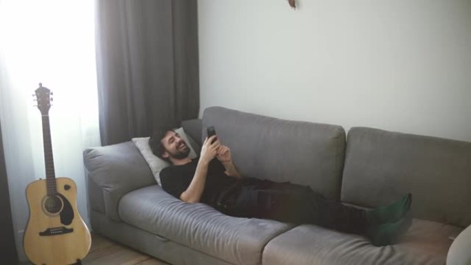 年轻帅哥用手机在沙发上放松，喜欢和朋友交流