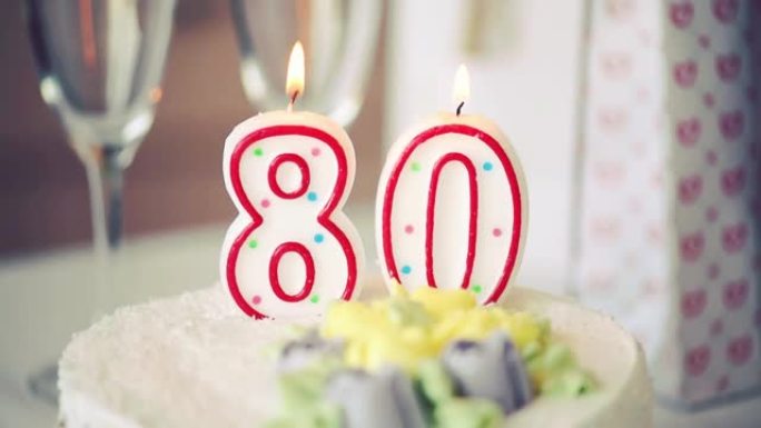 生日蜡烛作为80号80在桌上的甜蛋糕上，80岁生日，调色视频高清