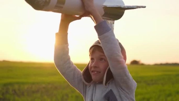戴着头盔的可爱的小男孩飞行员宇航员在日落野外夏季大自然中与玩具火箭一起奔跑。孩子大梦想飞行，宇航员，