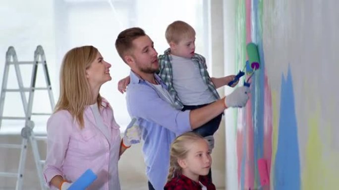 年轻的男女唐氏综合症男孩和女童在装修期间在室内用彩色油漆粉刷墙壁，微笑着看着相机