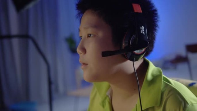 快乐的亚洲男孩使用耳机和PC电脑在夜间与朋友在家玩网络游戏，带led灯，生活方式理念。