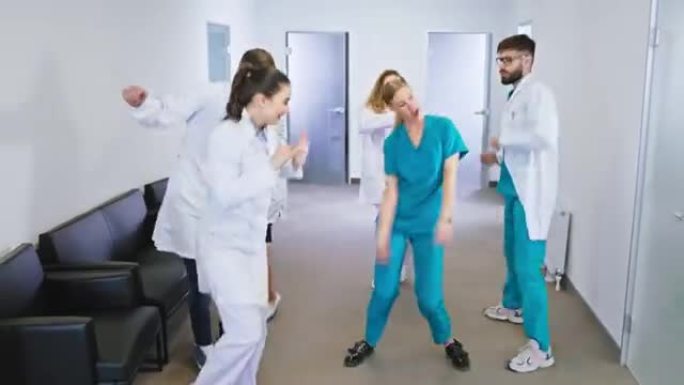 一群年轻成熟的医生和护士在现代医院走廊的镜头前兴奋地跳舞