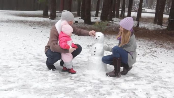 一对幸福的夫妇和一个小孩在冬季森林里堆雪人