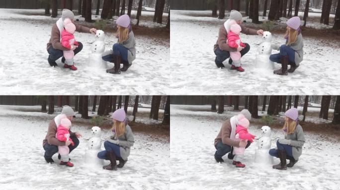 一对幸福的夫妇和一个小孩在冬季森林里堆雪人