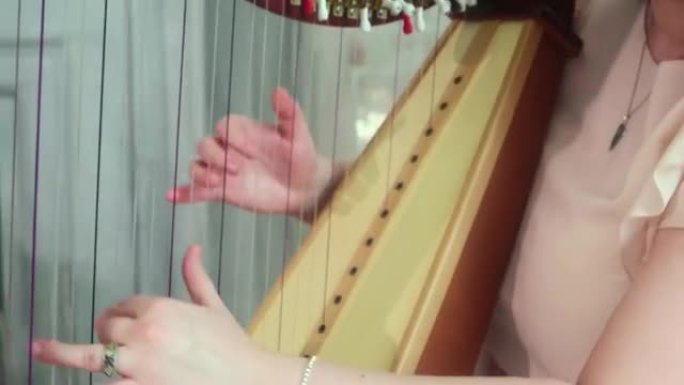 一个漂亮的女孩弹竖琴。用手放在女孩身上的全景。音乐艺术