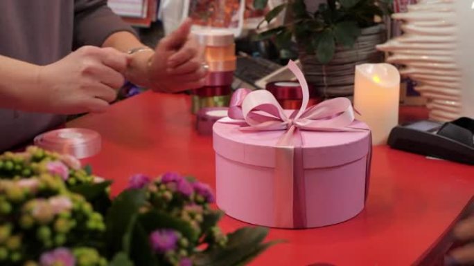卖家双手在商店里给客户圆形粉色礼物盒包装胶带。礼品店的买家手拿粉色丝带圆盒子。