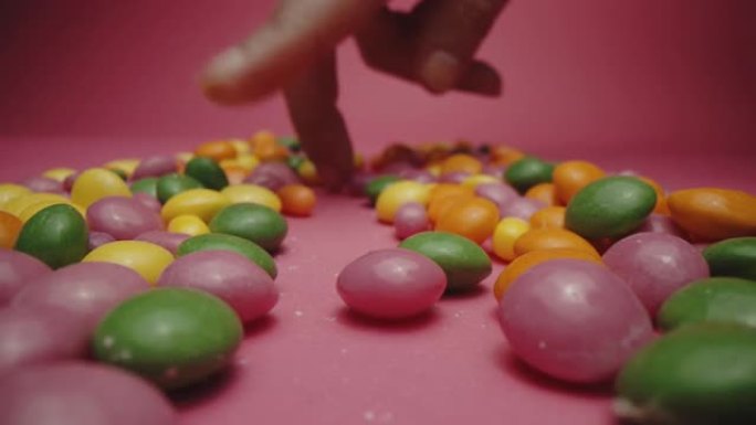 女性手指穿过粉红色背景上的一堆糖果